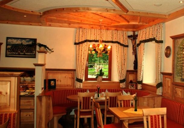 Ein gemütlicher Essbereich mit Holzmöbeln, roten gepolsterten Bänken, einem Fenster mit Vorhängen, einem Kronleuchter und einem Kruzifix an der Wand.