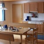 Eine Küche und ein Essbereich mit Holzschränken, einem Herd, einer Spüle und einem Holztisch, der mit Geschirr, Tassen und einer Teekanne für das Frühstück gedeckt ist.