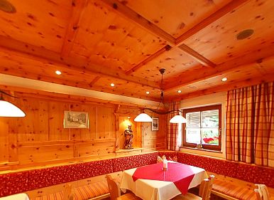 Holzgetäfeltes Esszimmer mit gepolsterten Sitzbänken, rot-weißer Tischdecke, Hängeleuchten, Fenster mit Vorhängen und gerahmter Wandkunst.