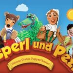 Über dem Text „Kasperl und Pezi“ sind vor einem blauen Himmel mit Wolken und einer Sonne bunte Puppen abgebildet, darunter ein Bär, ein Krokodil und menschliche Figuren.