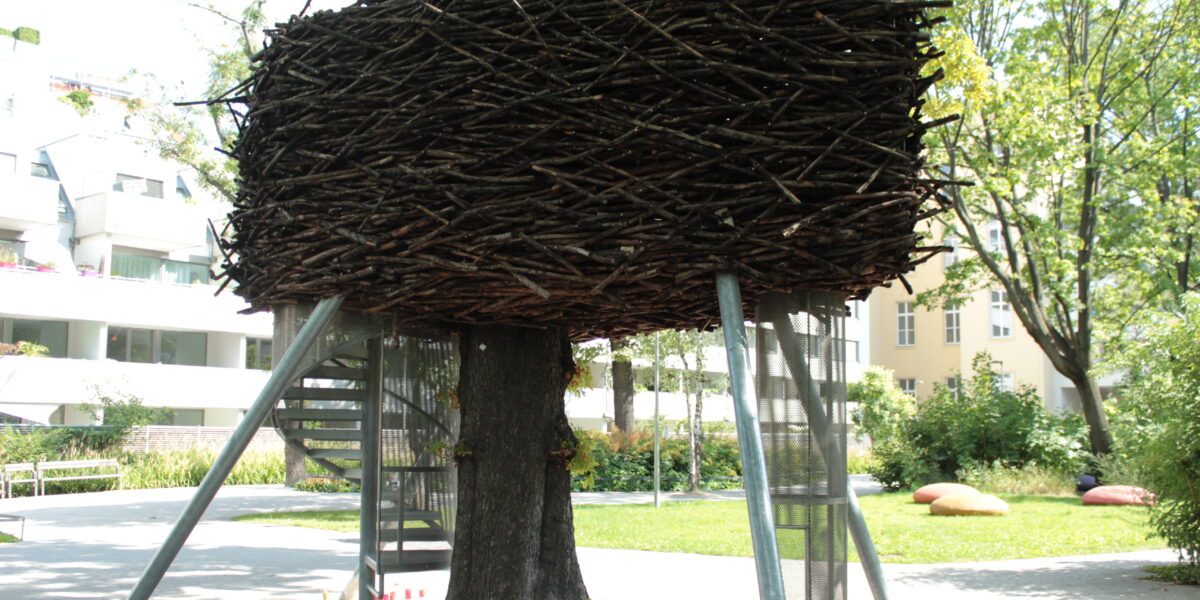 In einem Park im Freien wird ein großes künstliches Nest aus Stöcken um einen Baum herum gebaut und von Metallstangen gestützt.