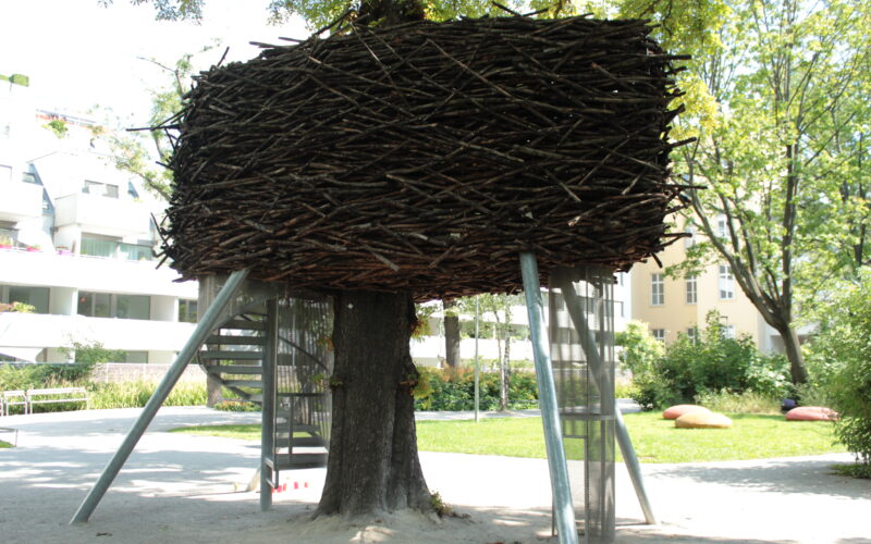 In einem Park im Freien wird ein großes künstliches Nest aus Stöcken um einen Baum herum gebaut und von Metallstangen gestützt.