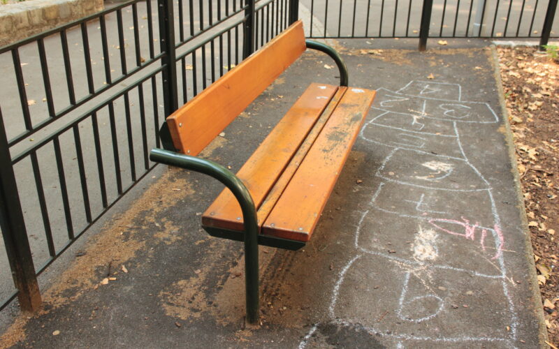 Eine hölzerne Parkbank auf einer gepflasterten Fläche neben einem mit Kreide gezeichneten Himmelfahrtskommando.