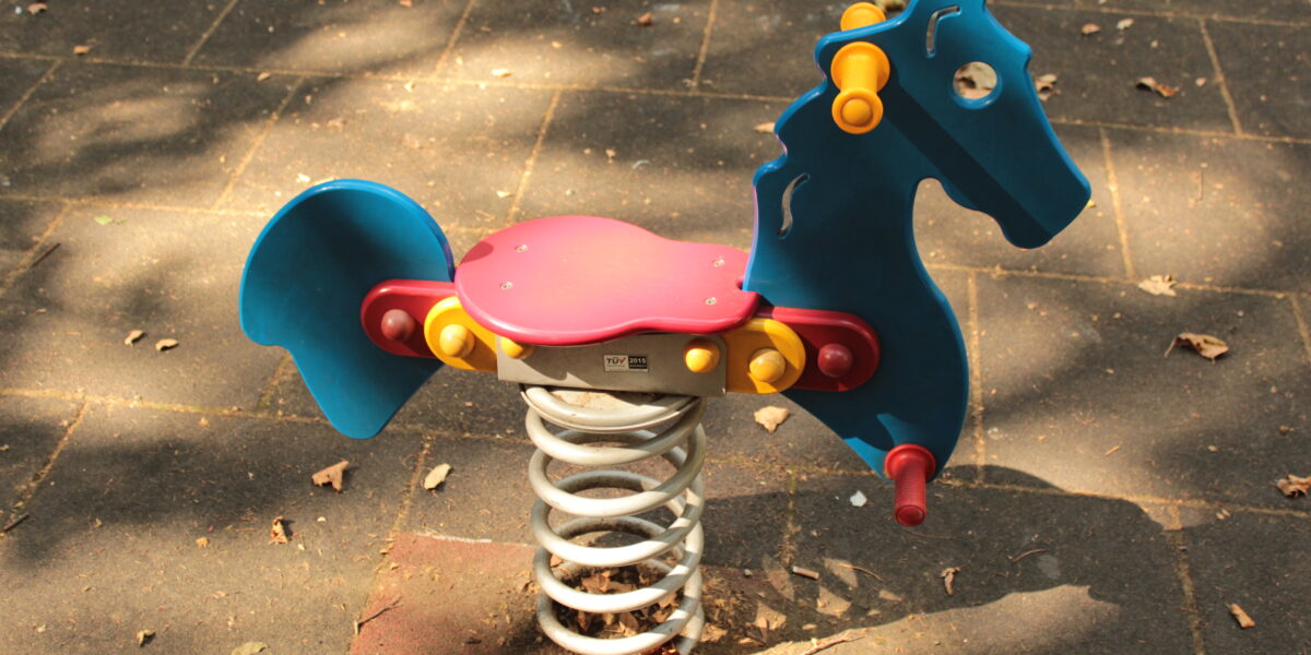 Ein blauer und roter Springreiter in Form eines Pferdes ist auf einem Spielplatz mit einem gefliesten Gummibelag installiert.