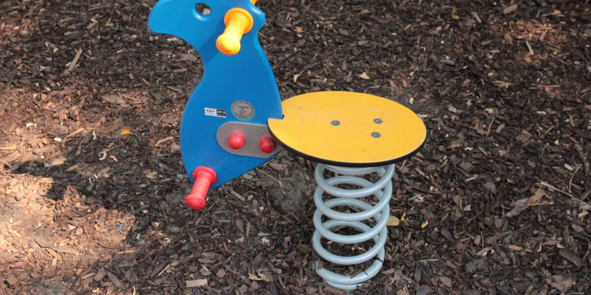 Blauer und gelber Spielplatz-Federreiter in Form eines Tieres, installiert auf braunem Mulchboden.