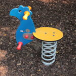 Blauer und gelber Spielplatz-Federreiter in Form eines Tieres, installiert auf braunem Mulchboden.
