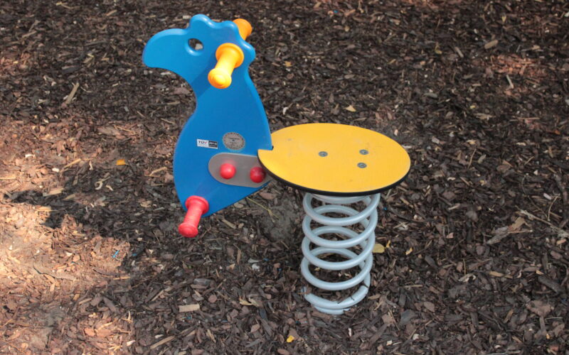 Blauer und gelber Spielplatz-Federreiter in Form eines Tieres, installiert auf braunem Mulchboden.