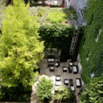 Luftaufnahme eines Innenhofs mit Terrassenbestuhlung, umgeben von grünen, mit Efeu bewachsenen Mauern und Bäumen.