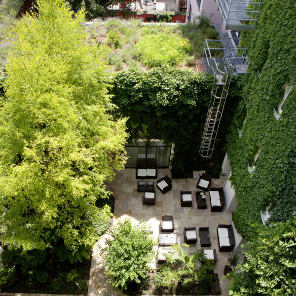 Luftaufnahme eines Innenhofs mit Terrassenbestuhlung, umgeben von grünen, mit Efeu bewachsenen Mauern und Bäumen.