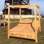Eine große Lounge-Sitzgruppe aus Holz im Freien mit einer Pergola-Struktur, beschriftet mit „Naturpark Leiser Berge“, auf Gras gelegen, mit einem Holzturm im Hintergrund.