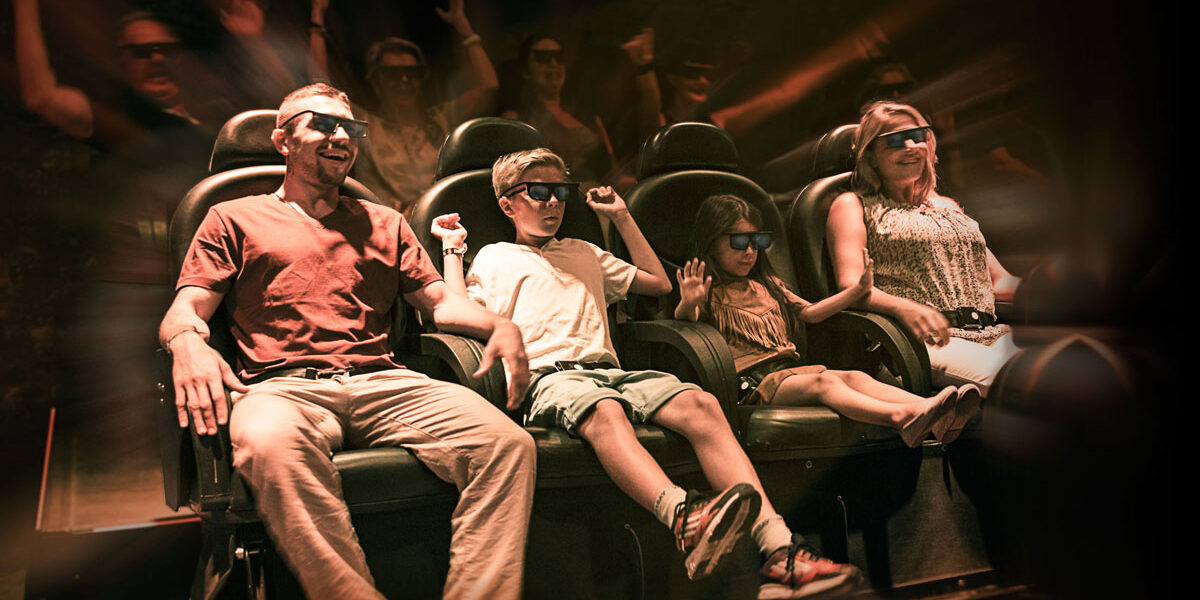 Vier Personen mit 3D-Brillen sitzen in den Sitzen des Bewegungssimulators und erleben eine immersive Fahrt mit dynamischen Lichteffekten und verschwommenen Bewegungen im Hintergrund.