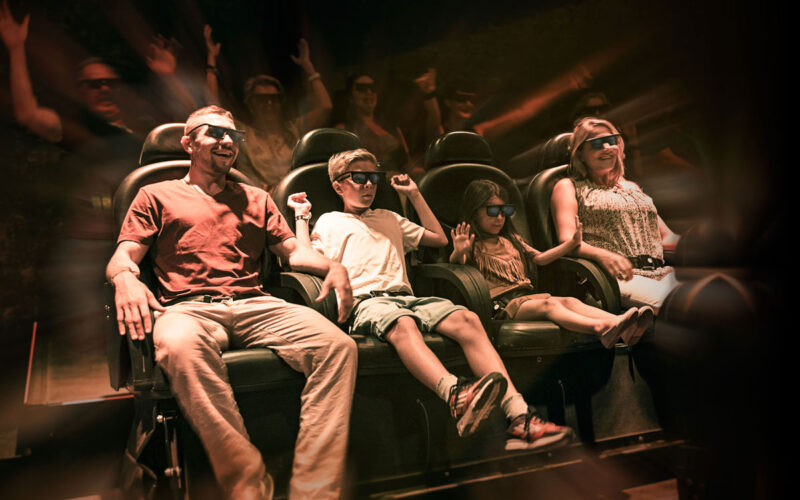 Vier Personen mit 3D-Brillen sitzen in den Sitzen des Bewegungssimulators und erleben eine immersive Fahrt mit dynamischen Lichteffekten und verschwommenen Bewegungen im Hintergrund.