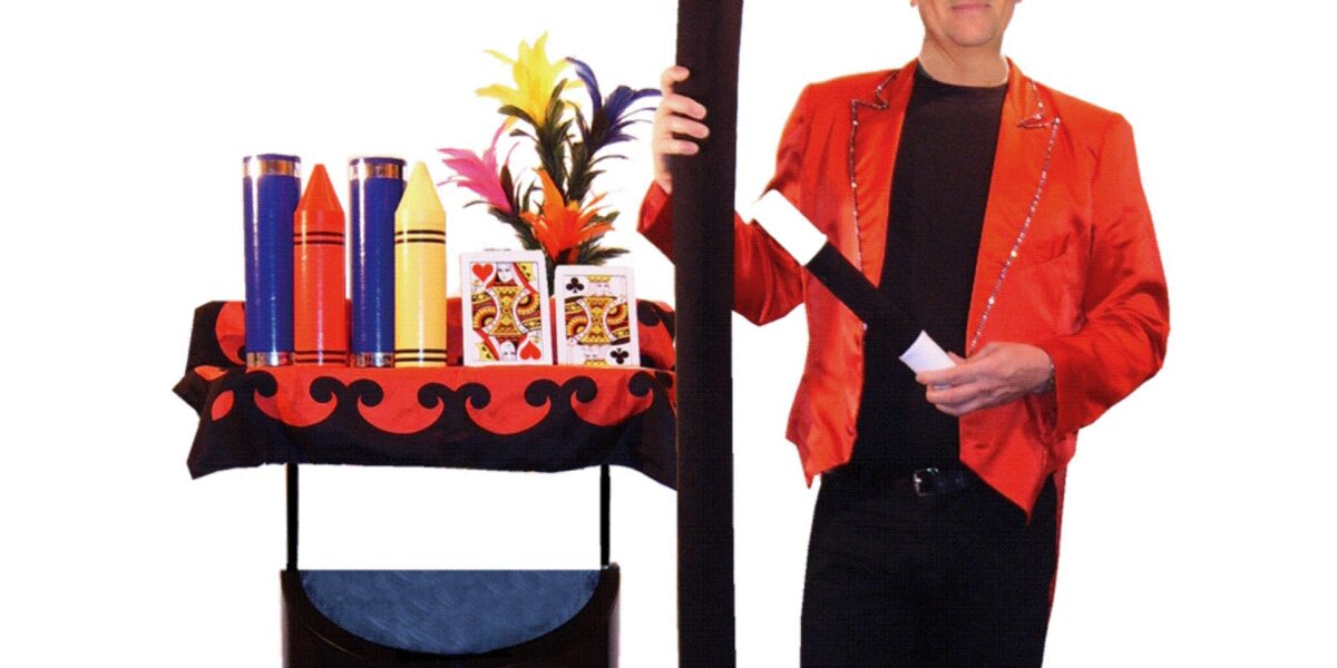 Ein Zauberer in einer roten Jacke steht neben einem Zaubershow-Wagen mit Requisiten und hält einen großen Zauberstab. Der Text darüber lautet "Power Magic mit Wolfgang der Zauberer im roten Frack.