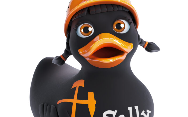 Eine schwarze Gummiente mit geflochtenem Haar, die einen orangefarbenen Bergmannshelm mit Stirnlampe trägt und mit der Aufschrift „Sally“ und einem Spitzhacken- und Hammersymbol an der Seite versehen ist.