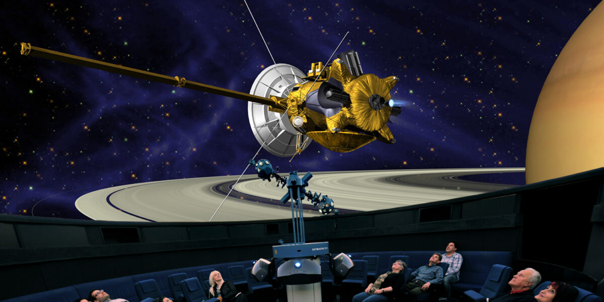 Die Besucher eines Planetariums sehen auf einem großen Kuppelbildschirm die Projektion eines Raumschiffs in der Nähe des Saturns und seiner Ringe.