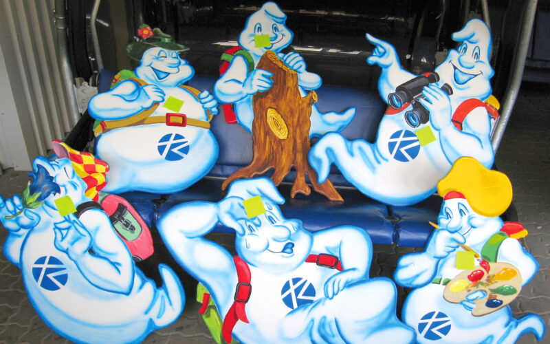 Sieben ausgeschnittene Cartoon-Geister, die jeweils unterschiedliche Gegenstände halten und als Vertreter verschiedener Berufe oder Hobbys gekleidet sind, sind auf einem blauen Sitz angeordnet.