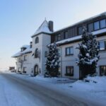 Ein großes, dreistöckiges Gebäude mit schneebedeckten Bäumen und Boden, das an einem klaren Wintertag an einer Straße steht.