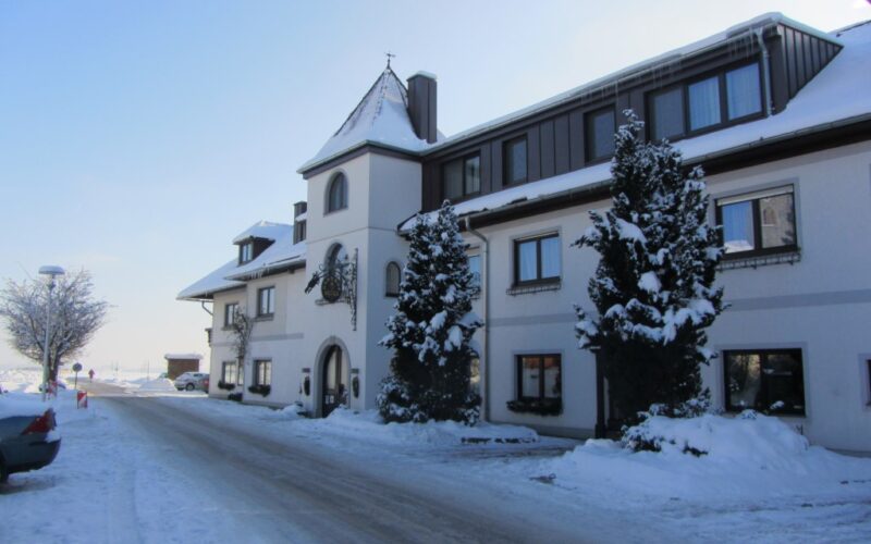 Ein großes, dreistöckiges Gebäude mit schneebedeckten Bäumen und Boden, das an einem klaren Wintertag an einer Straße steht.