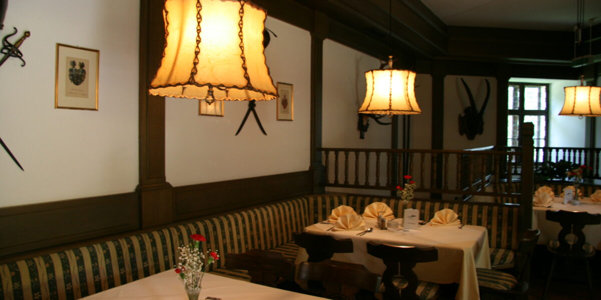 Ein gemütliches Restaurant mit gemusterten Bänken, weißen Tischtüchern, gefalteten Servietten, Blumenvasen und warmen Hängelampen an der Decke.
