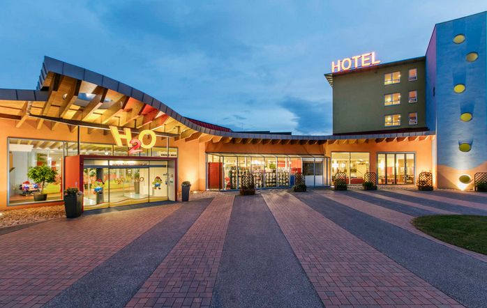 Modernes Hotel in der Abenddämmerung, mit großem "HOTEL"-Schild am Gebäude, gläsernem Eingang und gut beleuchteten Gehwegen.