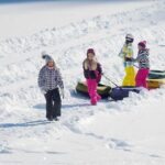 Kinder in Winterkleidung ziehen Schneeschläuche auf einem schneebedeckten Hang bergauf und bereiten sich auf eine weitere Fahrt vor.