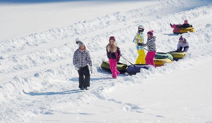 Kinder in Winterkleidung ziehen Schneeschläuche auf einem schneebedeckten Hang bergauf und bereiten sich auf eine weitere Fahrt vor.