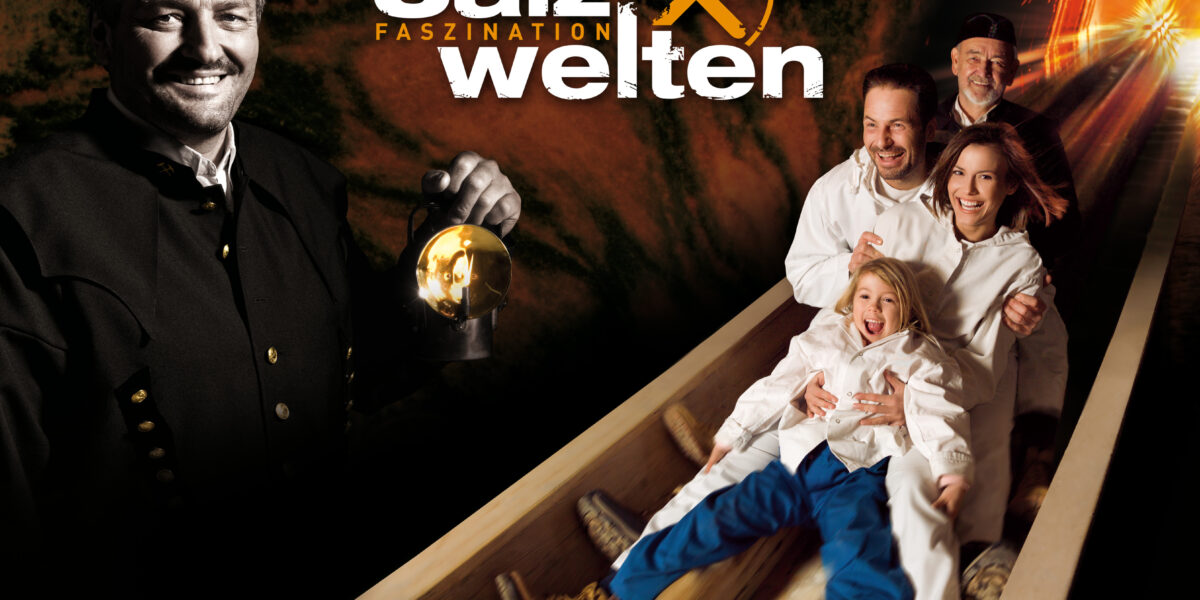 Ein lächelnder Mann in Bergmannskleidung hält eine Laterne; neben ihm rutscht eine Familie in weißer Kleidung eine Holzrutsche in einem Tunnel hinunter. Der Text lautet "Salzwelten Faszination.