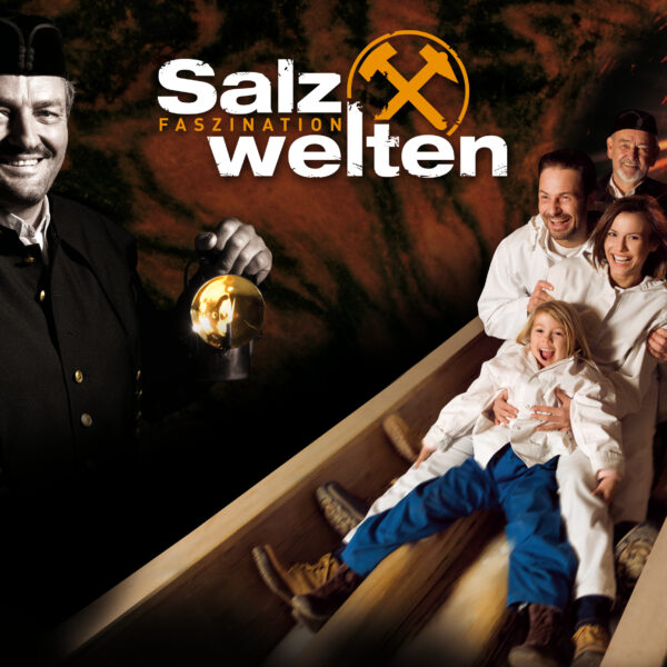 Ein lächelnder Mann in Bergmannskleidung hält eine Laterne; neben ihm rutscht eine Familie in weißer Kleidung eine Holzrutsche in einem Tunnel hinunter. Der Text lautet "Salzwelten Faszination.