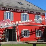 Ein rotes Gebäude mit grauen Fensterläden beherbergt das Feuerwehrmuseum; ein großes Schild an einer Leiter zeigt den Namen des Museums über dem Eingang an.