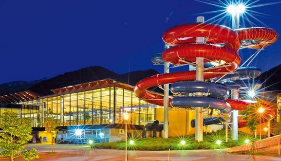 In einem nachts hell erleuchteten Gebäude befindet sich eine große Wasserrutsche im Freien mit roten und blauen Röhren, die sich um das Gebäude winden.