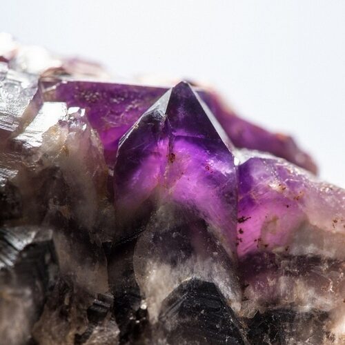 Nahaufnahme eines Amethystkristallclusters mit scharfen violetten Spitzen, die aus einer rauen, felsigen Basis hervortreten.