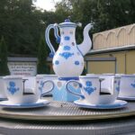 Ein sich drehendes Vergnügungspark-Fahrgeschäft als Teeservice mit großen Teetassen und einer Teekanne mit blauen Blumenmustern auf einer Metallplattform.