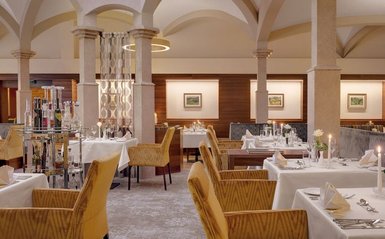 Elegantes Restaurantinterieur mit gewölbten Decken, gelb gepolsterten Stühlen, weißen Tischdecken, gedeckten Tischen und gerahmten Kunstwerken an den Wänden.