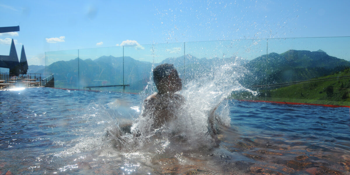 Eine Person spritzt mit Wasser, während sie in einem Infinity-Pool im Freien spielt, mit Bergen im Hintergrund.