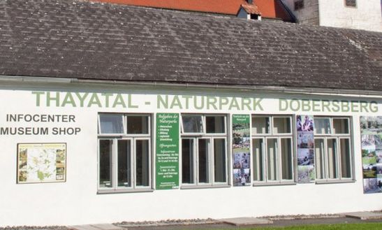 Ein weißes Gebäude mit der Aufschrift "Thayatal-Naturpark Dobersberg" mit Schildern für ein Infozentrum und einen Museumsshop sowie mehreren Fenstern und Plakaten an der Wand.