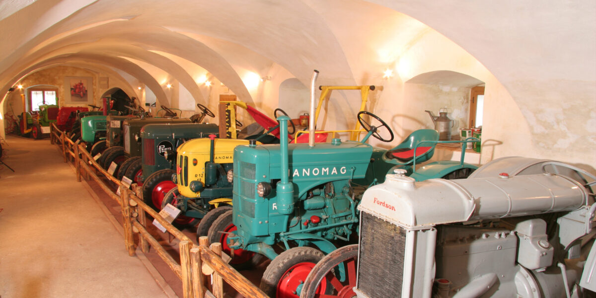 Eine Reihe von Oldtimer-Traktoren unter gewölbten Decken, die durch ein Holzgeländer vom Gehweg getrennt sind.