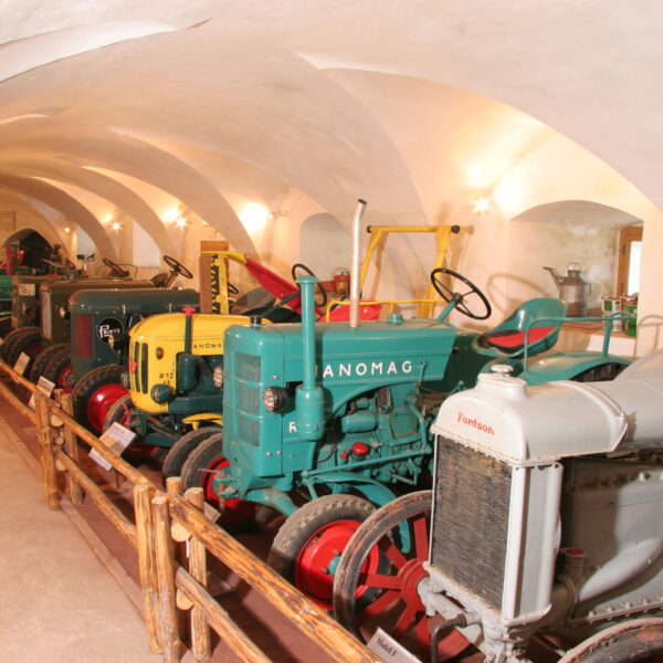 Eine Reihe von Oldtimer-Traktoren unter gewölbten Decken, die durch ein Holzgeländer vom Gehweg getrennt sind.