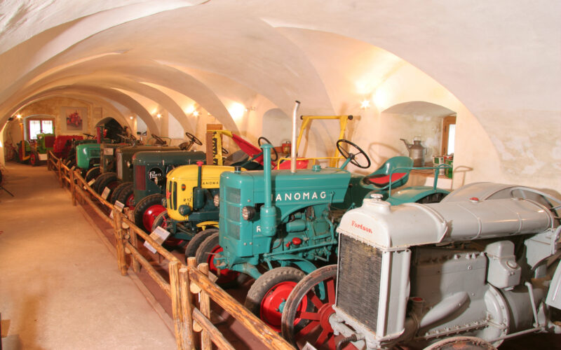 Eine Reihe von Oldtimer-Traktoren unter gewölbten Decken, die durch ein Holzgeländer vom Gehweg getrennt sind.