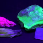 Eine Sammlung von Mineralien, die unter ultraviolettem Licht in verschiedenen Neonfarben leuchten, darunter leuchtend grüne, rosa und violette Farbtöne.