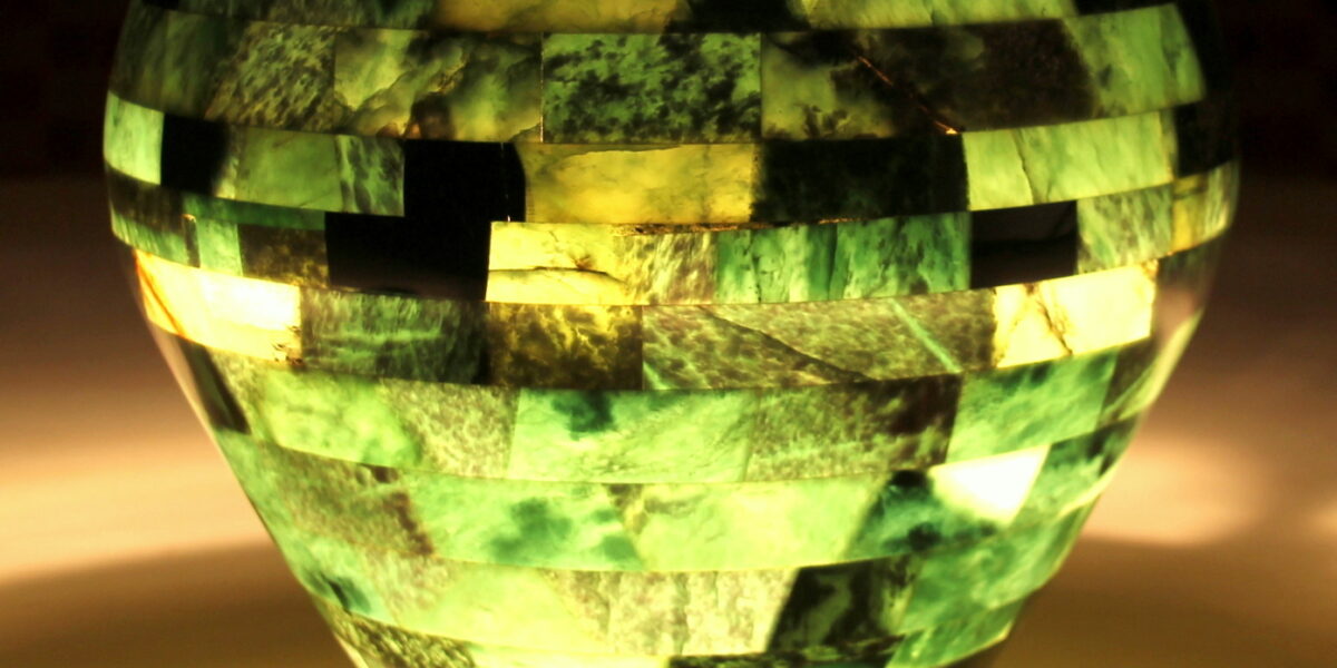 Eine mosaikartige grüne und gelbe Lampe strahlt ein sanftes Licht aus, das die Umgebung auf einer hellen Fläche beleuchtet.
