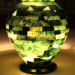 Eine mosaikartige grüne und gelbe Lampe strahlt ein sanftes Licht aus, das die Umgebung auf einer hellen Fläche beleuchtet.