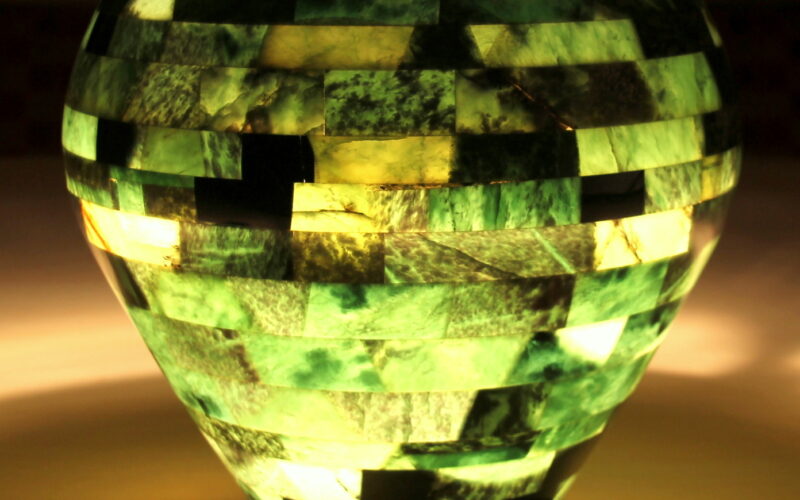 Eine mosaikartige grüne und gelbe Lampe strahlt ein sanftes Licht aus, das die Umgebung auf einer hellen Fläche beleuchtet.