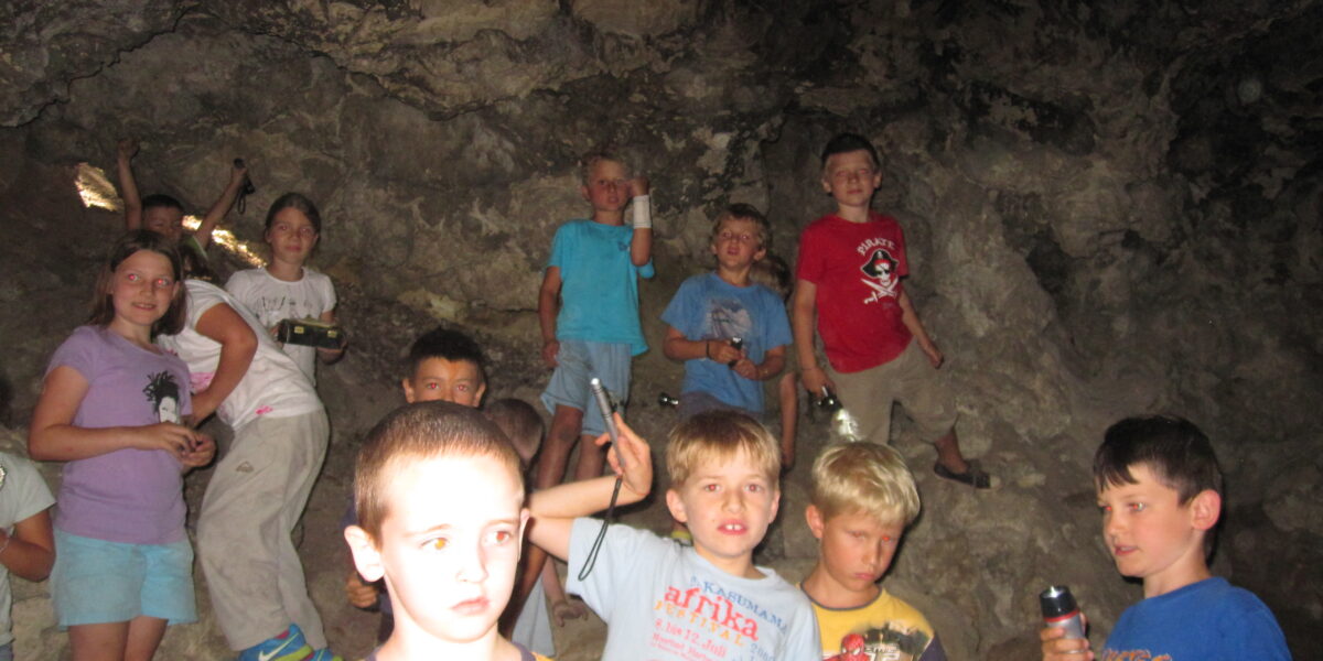 Eine Gruppe von Kindern steht in einer felsigen Höhle, einige halten Taschenlampen in der Hand und schauen in die Kamera.