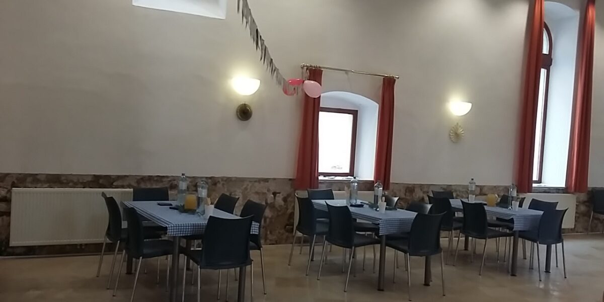 Ein Essbereich mit vier Tischen, die mit karierten Tüchern bedeckt, mit Flaschen und Gläsern gedeckt und mit rosa Luftballons und einer Wimpelkette dekoriert sind.