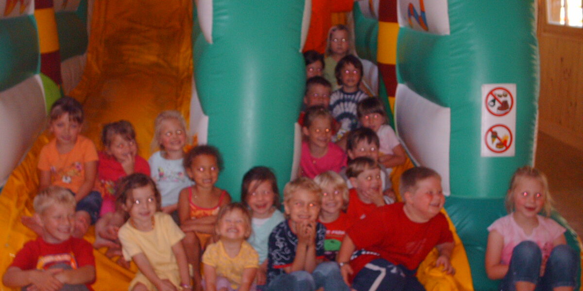 Eine Gruppe von Kindern sitzt für ein Foto am Fuße einer aufblasbaren Rutsche in einem Spielbereich und posiert.