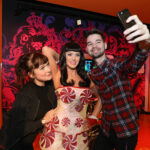 In einem hell erleuchteten Ausstellungsraum posieren zwei Personen für ein Selfie mit einer Wachsfigur, die ein mit roten und weißen Pfefferminzmotiven verziertes Kleid trägt.