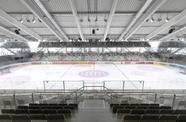 Leere Eishockeyhalle mit sichtbaren Sitzplätzen, übersichtlichen Banden und Werbung auf der Eisfläche und an den Wänden.