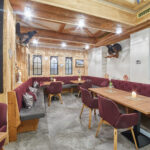 Ein gemütlicher Restaurantbereich mit kastanienbraunen, gepolsterten Sitzbänken, Holztischen, dekorierten Wänden und einer Kreidetafel, auf der ein deutscher Gruß steht.