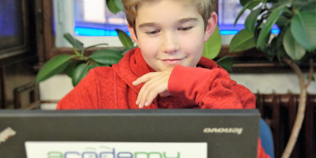 Ein junger Mensch in einem roten Kapuzenpulli sitzt vor einem Laptop mit einem „Acodemy“-Aufkleber, blickt auf den Bildschirm und stützt sein Kinn auf die Hand.