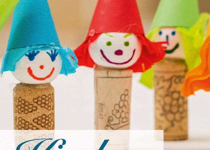 Drei Korkpuppen mit bunten Papierhüten und bemalten Gesichtern stehen aufrecht auf einem Tisch. Der deutsche Text lautet: „Kindergeburtstag im KunstTRAUMstift.“.